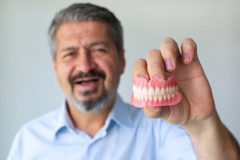 An old gray-haired man holds his denture